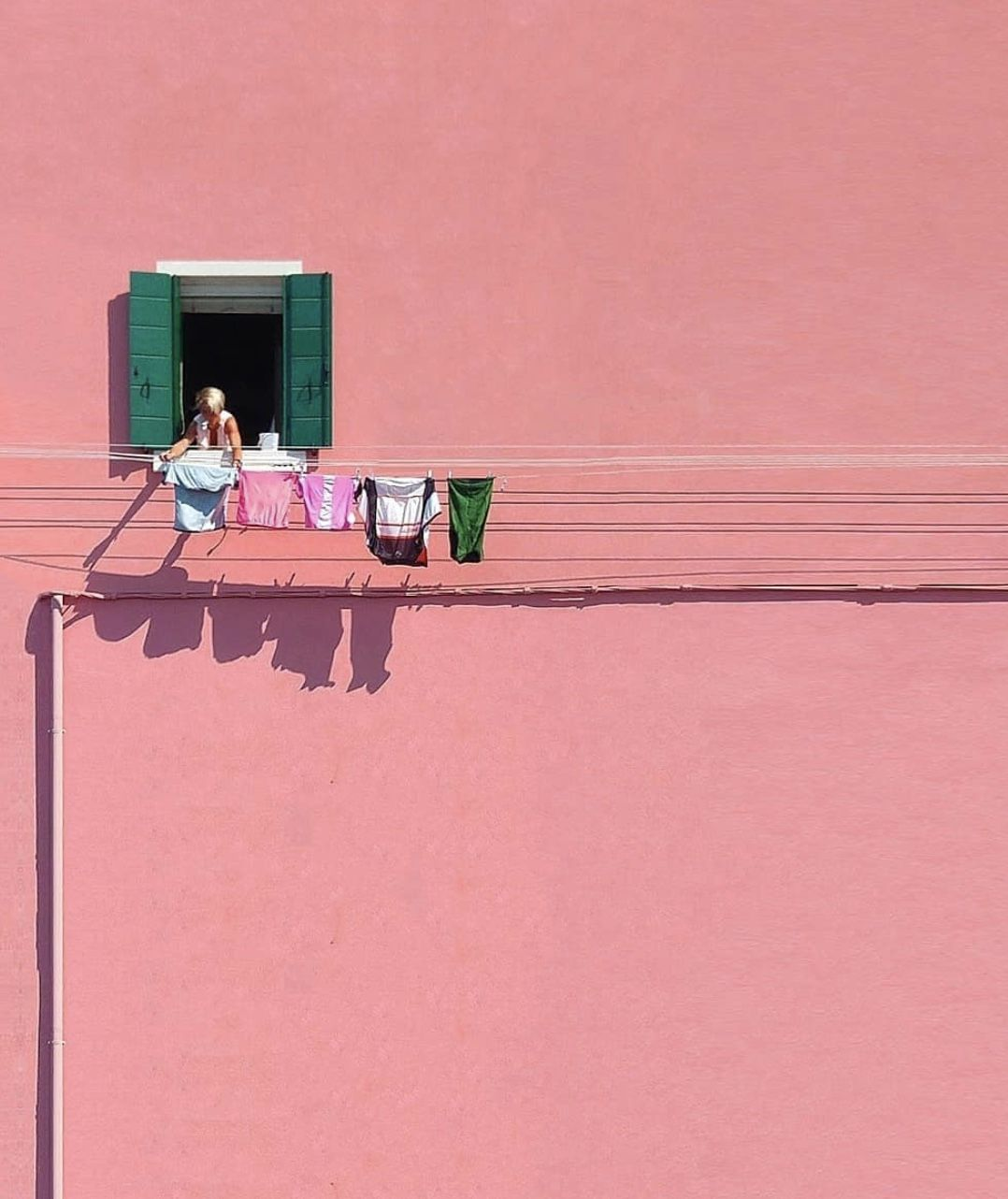 Pink building facade with a green-shuttered window and laundry drying on a line